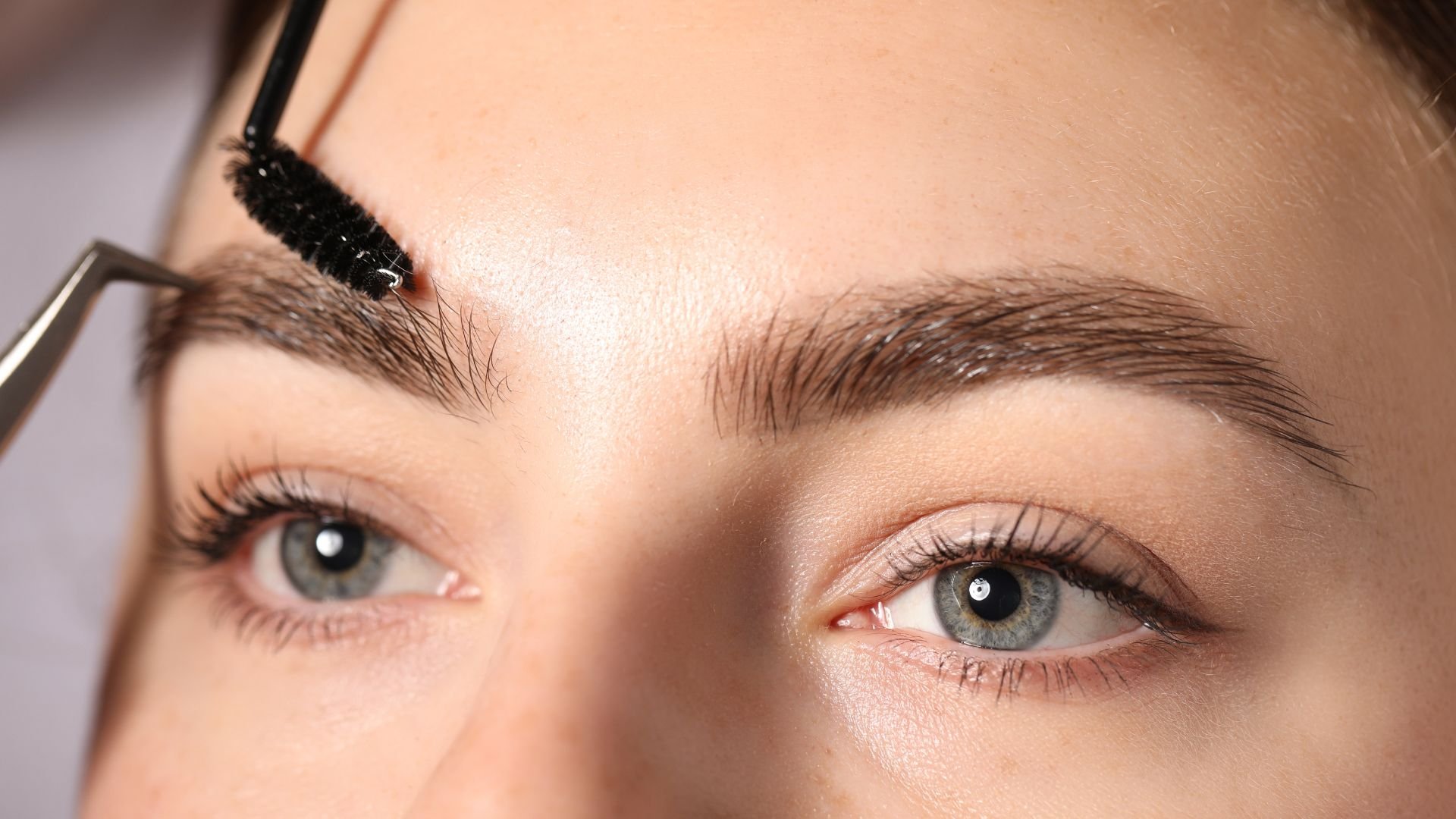 Closeup of eyebrow makeup application with mascara brush and tweezers