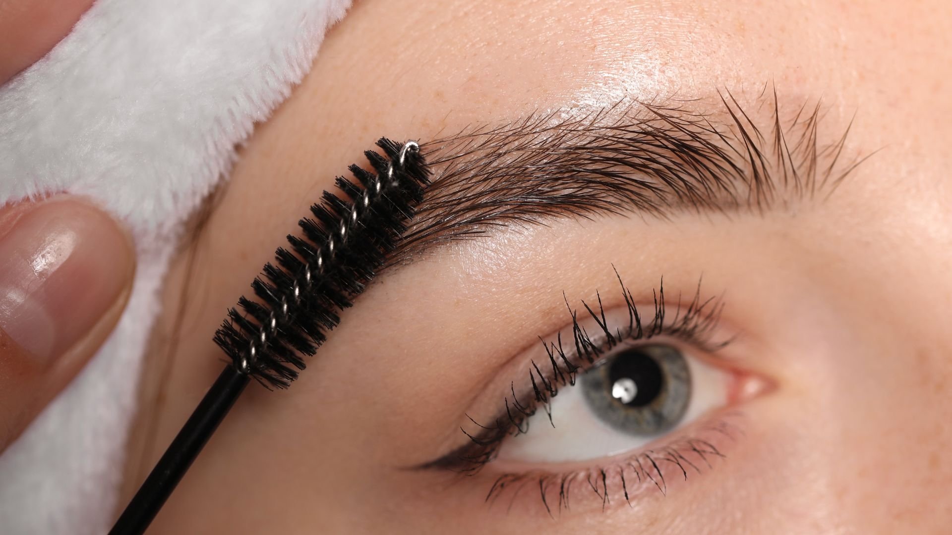 Makeup brush applying mascara to long eyelashes and groomed eyebrow