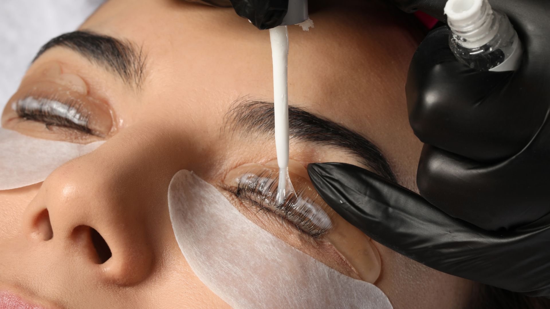 Eyelash lift procedure with gloved hands applying chemical solution